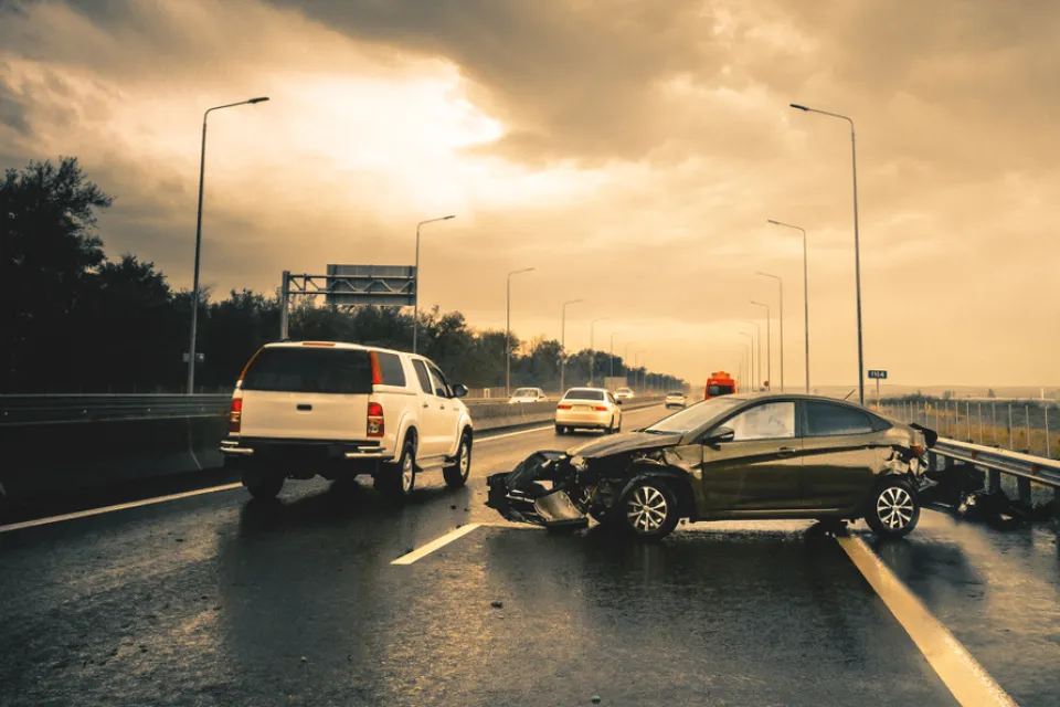 Small black car with mangled bumper sitting sideways on an asphalt road